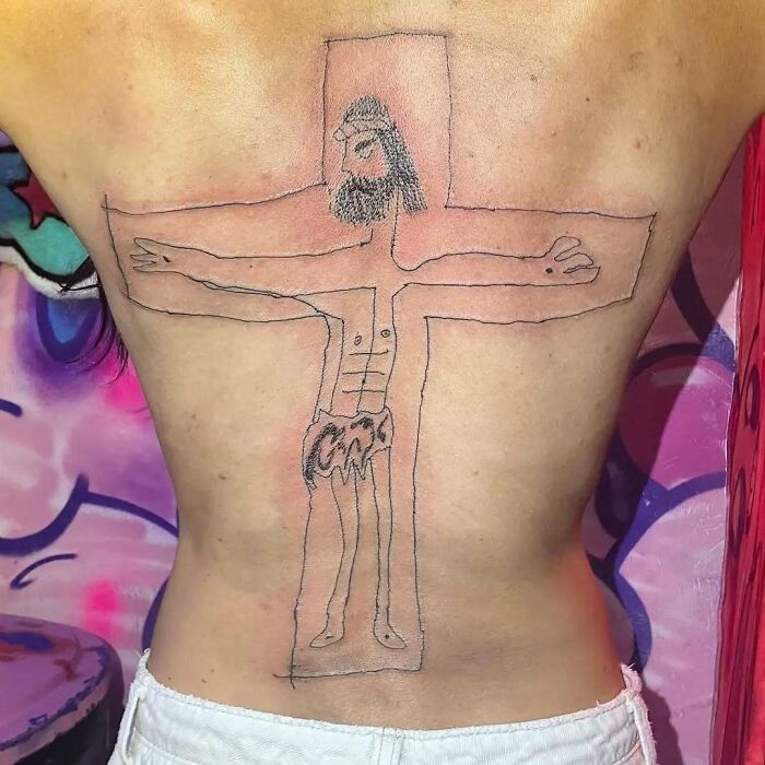 A hilariously bad tattoo depicting a stick figure on a cross, showcasing poor art skills on a person's back.