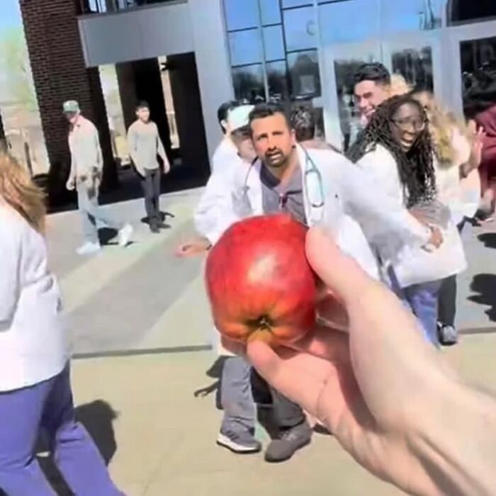 Person holding an apple as a group of people in lab coats run toward them, creating a random cursed image.