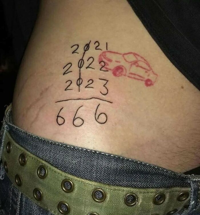 Bad tattoo featuring years, a red car sketch, and the number 666 on skin above a studded belt.