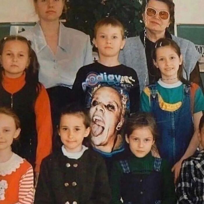 Children in a group photo, one wearing a shirt with a graphic face. Cursed image with unexplained elements.