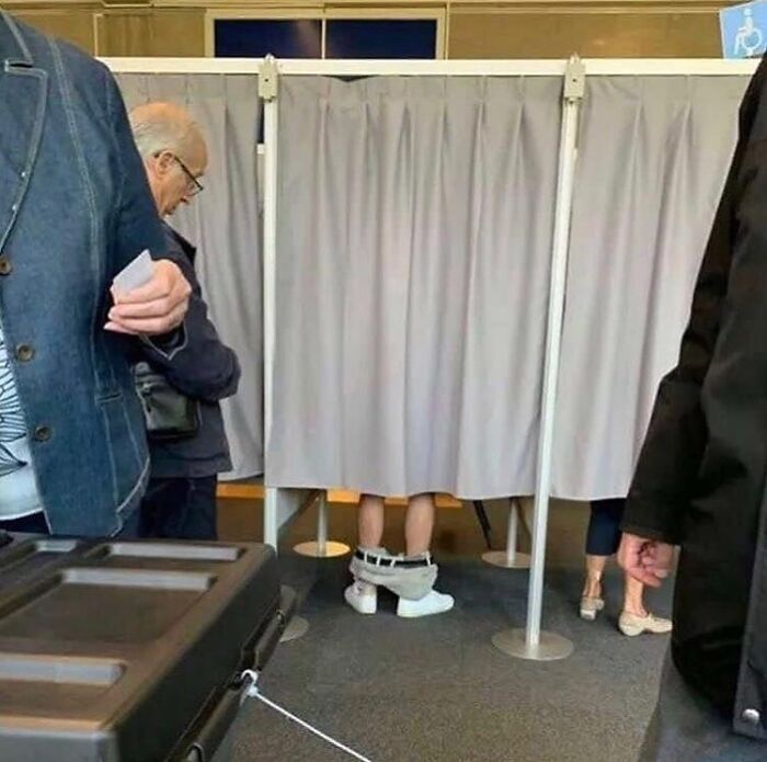 A person wearing large shoes and pants around ankles in a voting booth, illustrating a random cursed image.