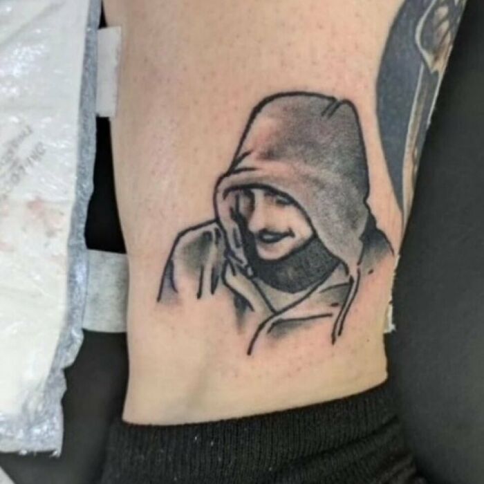 Tattoo of a hooded figure on forearm, showcasing a permanent ink mistake.