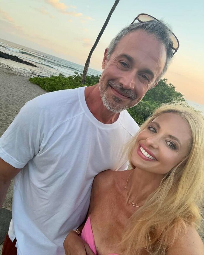 Man and woman smiling on a beach at sunset during a celebrity encounter in a relaxed outdoor setting.
