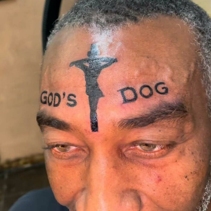 Forehead tattoo reads "God's Dog" with a silhouette of a cross, highlighting a permanent mistake on the body.