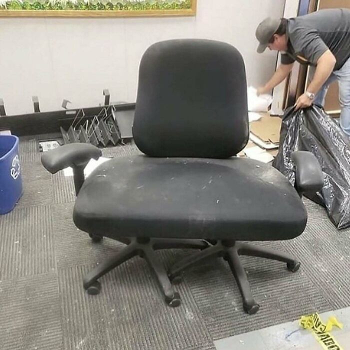 Oversized black office chair with a man in the background cleaning.