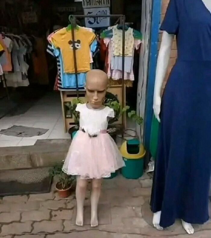 Bald mannequin in a pink dress outside a clothing store, showcasing a humorous setup from a popular IG page.