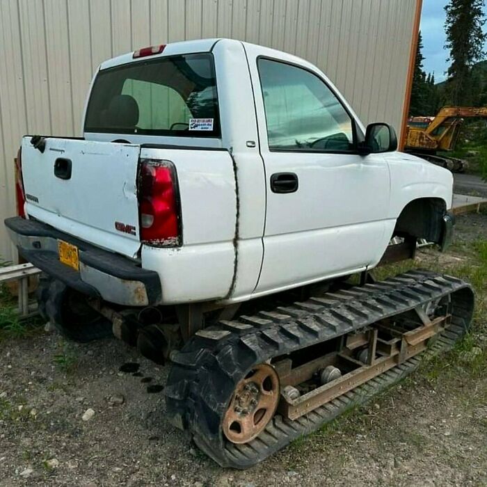 White truck with tank-style tracks on the ground, parked outside a metal building.
