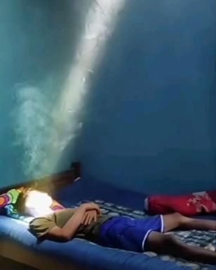 A person lying on a bed with sunlight dramatically illuminating their face in a dim room.