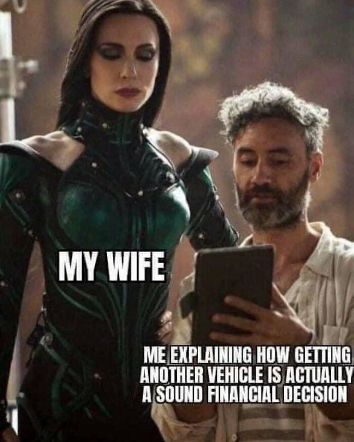 Man showing tablet to woman in superhero costume, joking about cars as a financial decision.