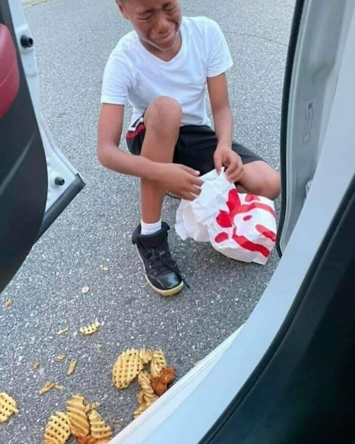 Child crying beside a car, holding a fast-food bag with spilled waffle fries on the ground.