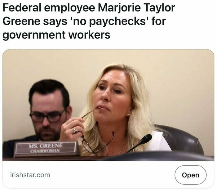 A woman at a meeting, labeled as chairwoman, with a nameplate in focus, discusses government worker paychecks.