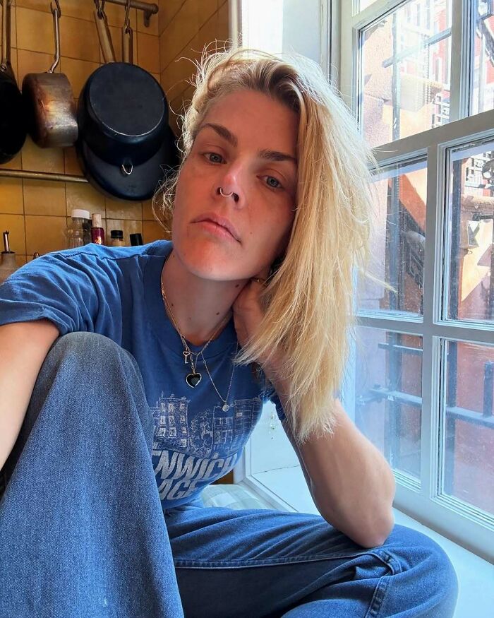 Blonde woman in casual attire sitting by a window, showcasing celebrity moments in an everyday setting.