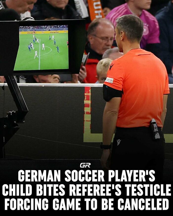 Referee in orange jersey reviews soccer video footage at stadium.