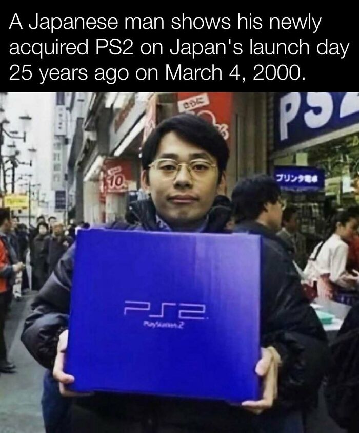 Man holding PS2 box on Japan launch day, March 4, 2000, surrounded by busy street scene.