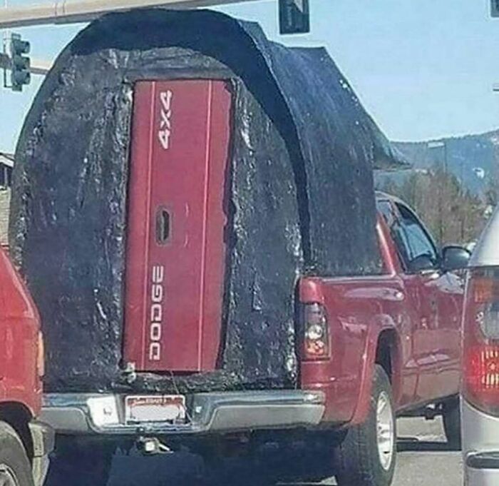 Red Dodge truck with a humorous makeshift camper, showcasing funny car meme creativity on the road.