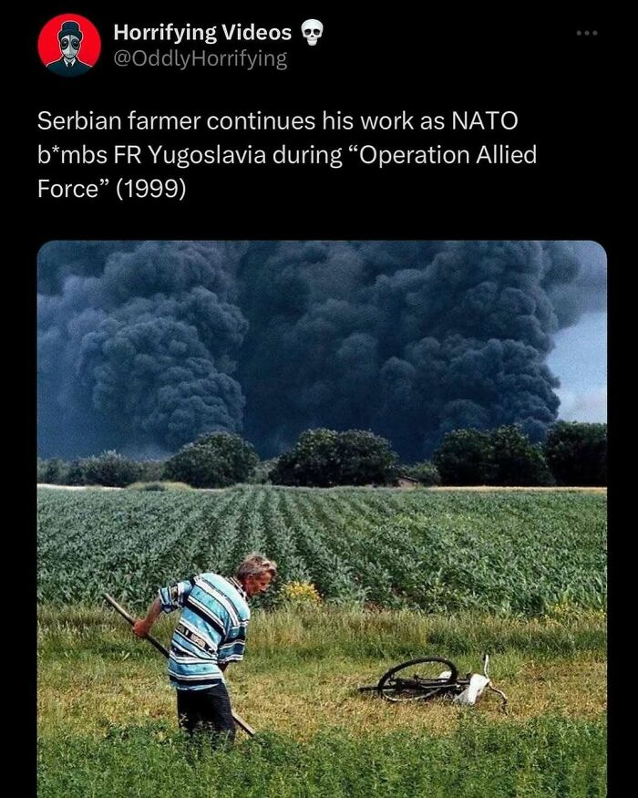 Serbian farmer works in field with massive smoke cloud from bombing in the background, creating an unnerving scene.