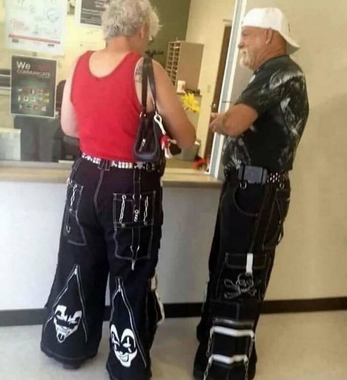Two people wearing unique black pants with graphic designs standing at a counter.