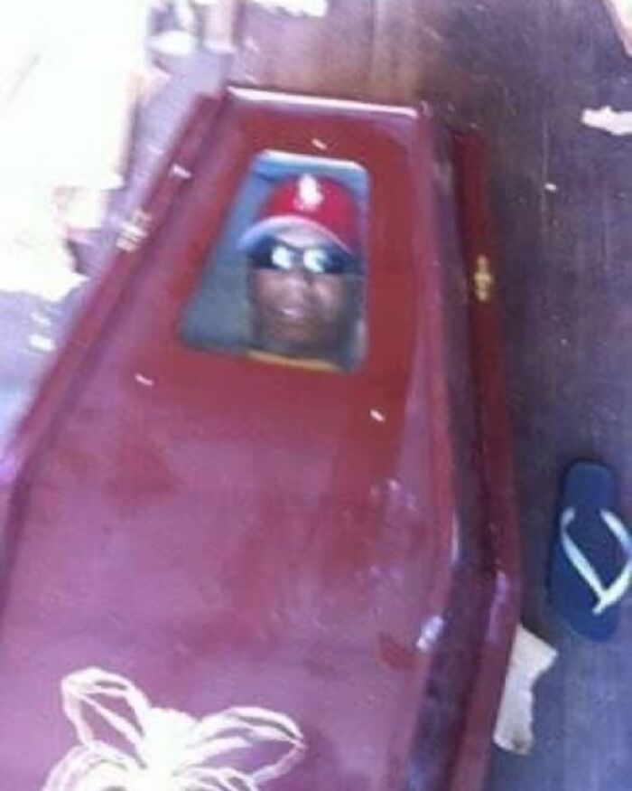 Person in a red cap and sunglasses peeks humorously from a closed wooden coffin, embodying a "literally hardest posts" vibe.