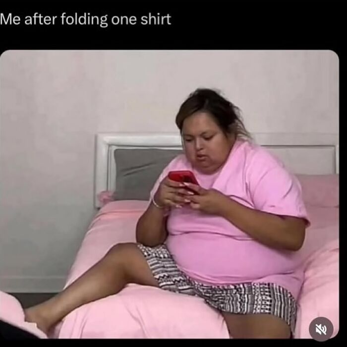 Person in pink shirt relaxing on bed with phone, captioned "Me after folding one shirt," conveying a funny meme moment.