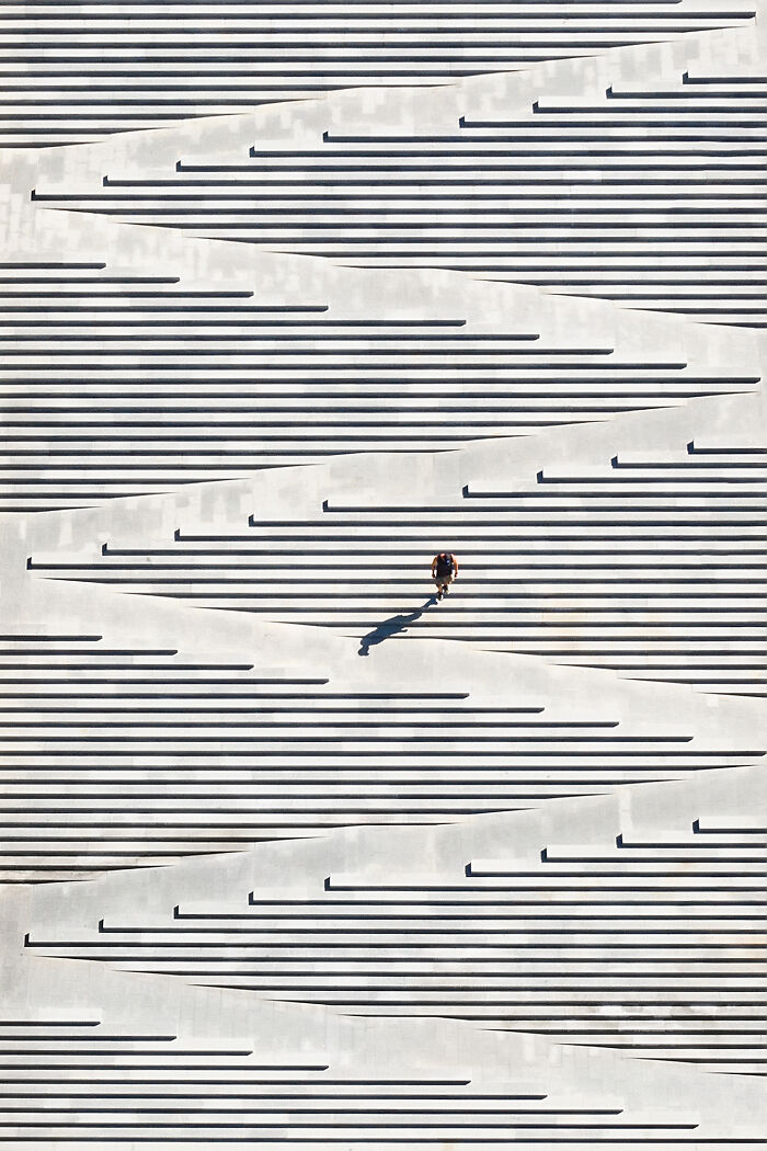 Aerial image showcasing a person walking on a minimalist concrete structure with geometric shadows and patterns.