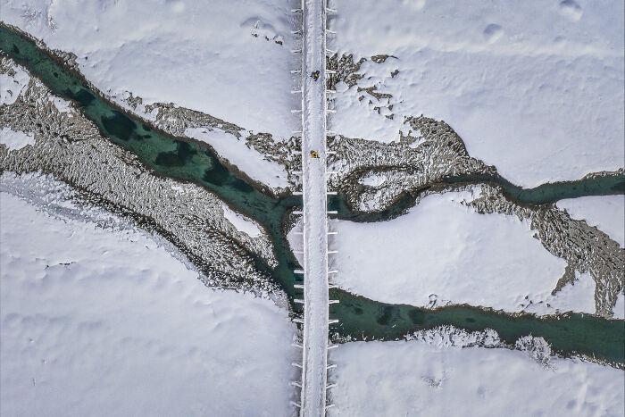 Aerial image of a snow-covered landscape with a bridge crossing a winding river in a unique perspective.