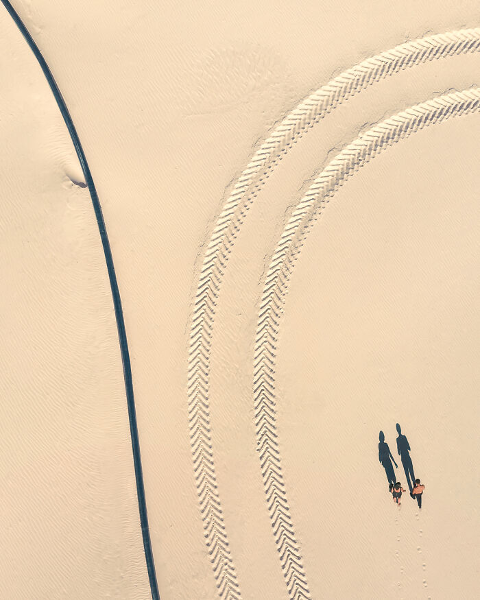 Aerial image capturing vehicle tire tracks and two people walking on light sandy terrain from a whole new perspective.