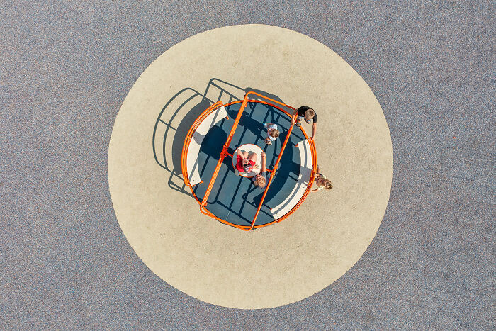Aerial image of children playing on an orange roundabout in a circular playground area showcasing a new perspective.