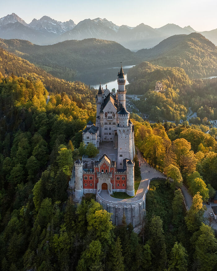 Aerial image of a historic castle surrounded by forested hills and mountains, showcasing the world from a new perspective.