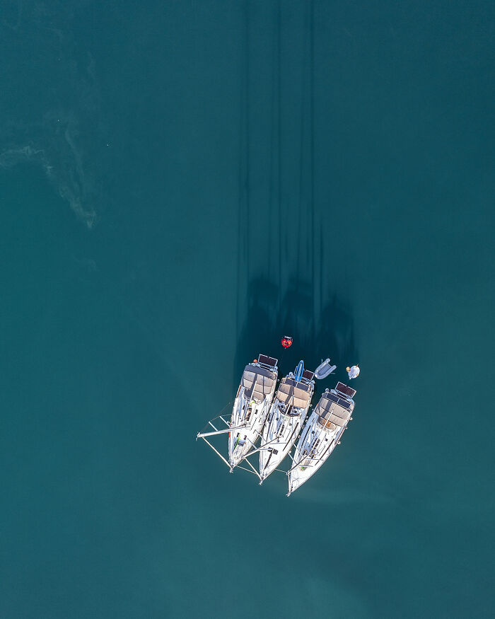Aerial image of three sailboats anchored closely together on calm, deep blue water showcasing world from a new perspective.