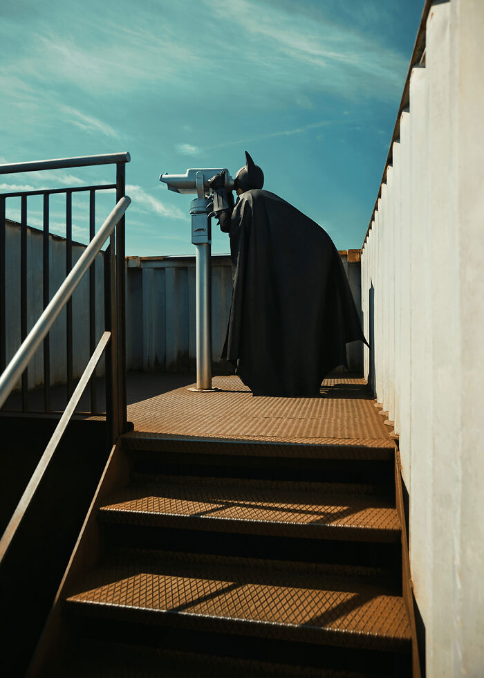 Batman observing through a telescope on a rooftop, attempting to live a normal life.