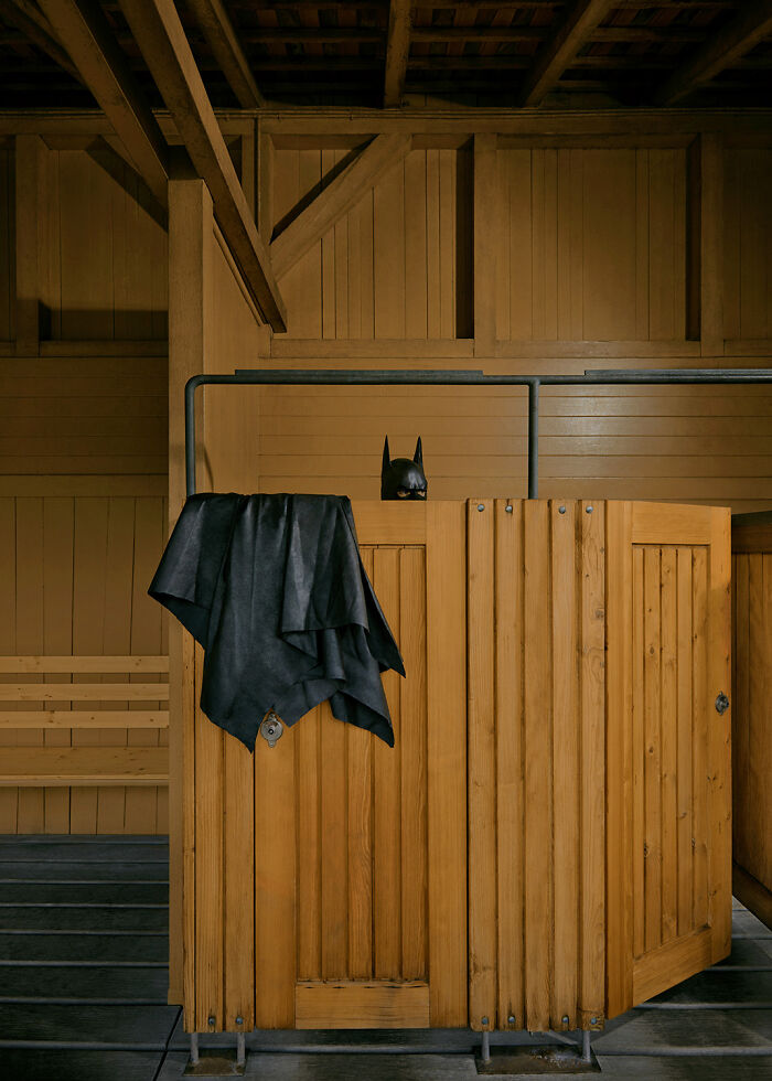 Batman mask and cape hang above a wooden locker in an everyday setting.