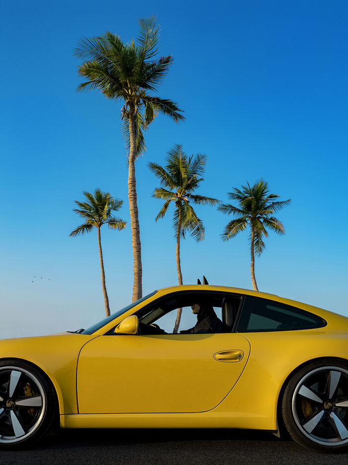 Batman in a yellow car under palm trees, embracing normal life.