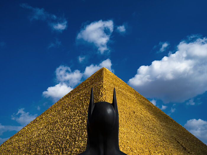 Batman standing before a massive pyramid under a clear blue sky.