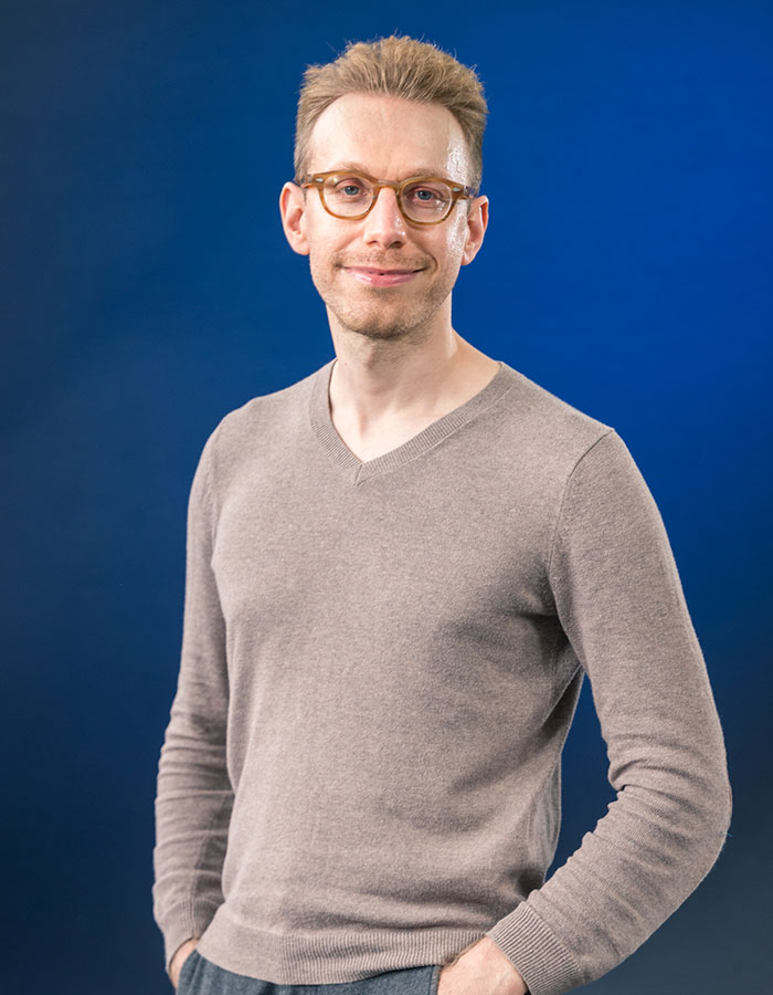 A person in a beige sweater and glasses stands against a blue background, embodying real-life superpowers.