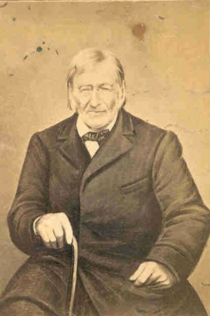 Sepia-toned rare photo of a famous historical figure sitting with a cane, wearing a dark coat and bow tie.