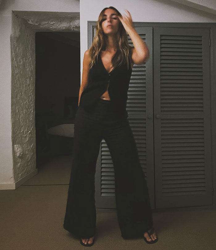 Woman in a black outfit striking a pose in a dimly lit room, capturing unglamorous red carpet moments.
