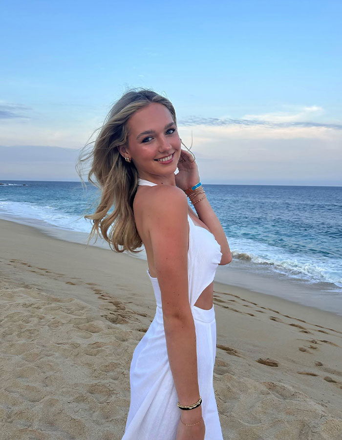 Young woman in a white dress posing on a beach at sunset.