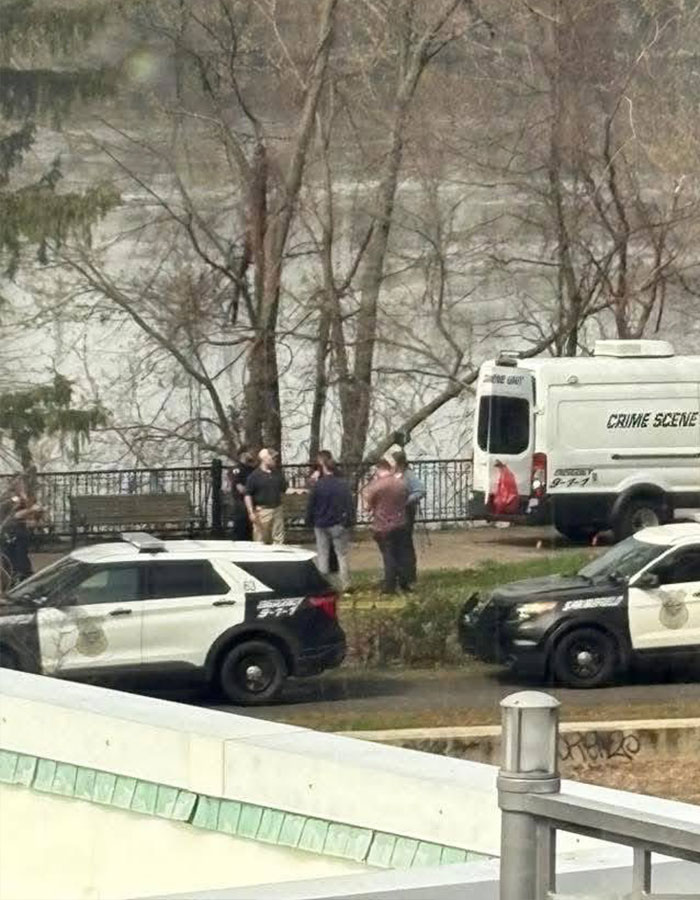 Crime scene investigation with police vehicles and officers near wooded area in New England.