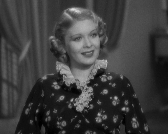 Young child actor in a vintage film, wearing a floral dress with a ruffled collar, smiling warmly.