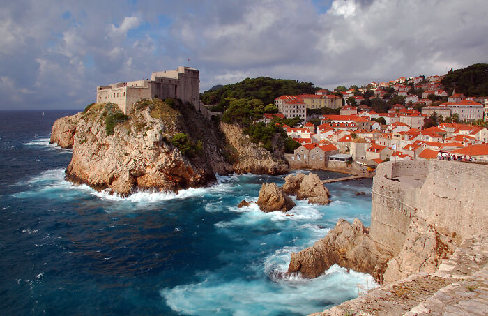 Historic coastal vista with a fortress overlooking the rugged shoreline and vibrant sea waves under a cloudy sky.