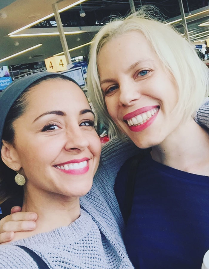Two women smiling at the camera in a busy indoor setting.