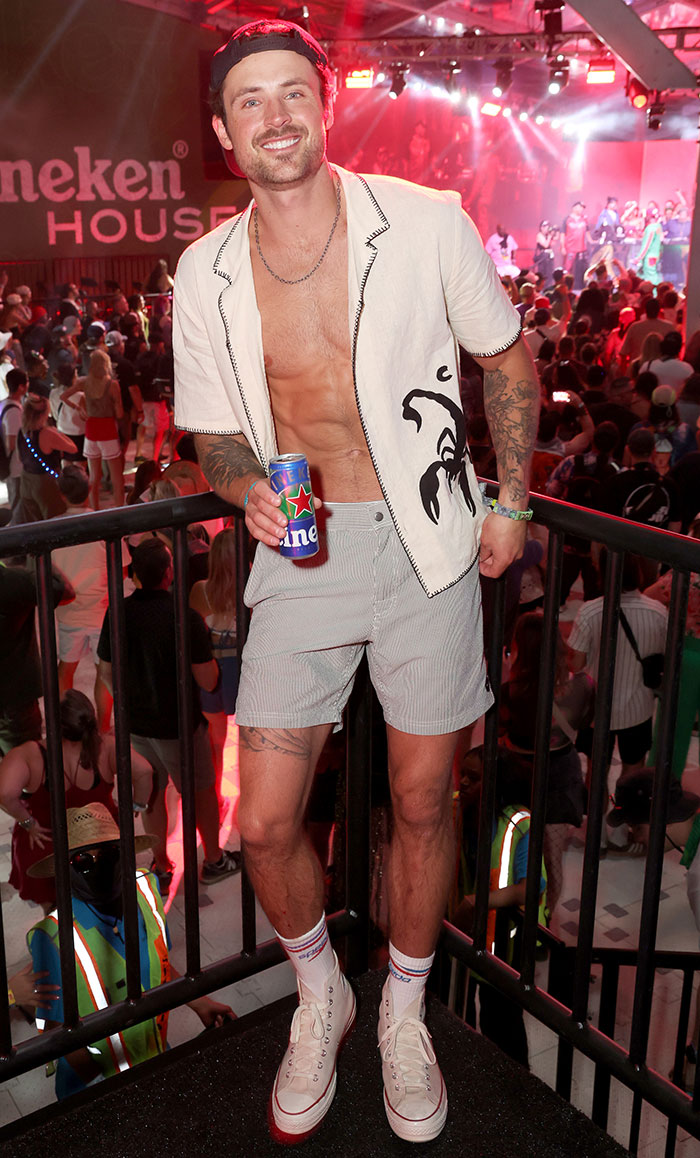 Man in festival attire at Coachella 2025, holding a drink, with crowd in background, highlighting worst dressed celebrities.