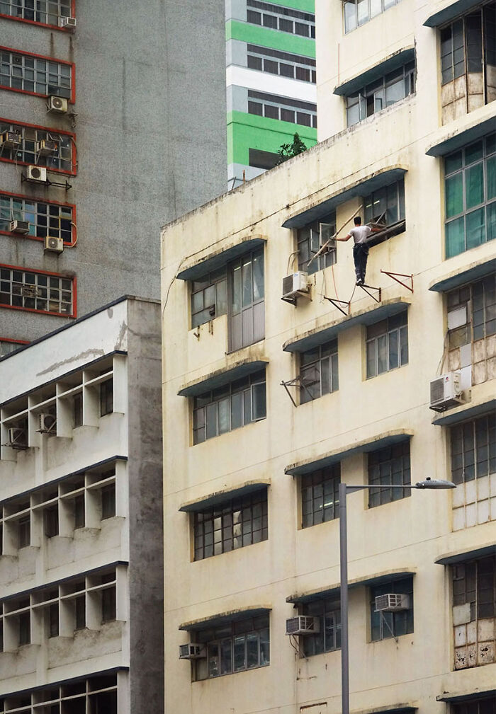 Equilibrium, 2023 - A Man Is Holding A Bamboo Pole With One Hand While Balancing On The Building's Facade