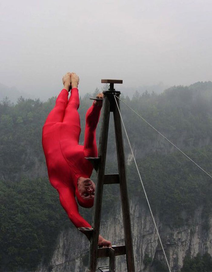 Man in red suit performs daring acrobatic feat on outdoor structure, showcasing real-life superpowers that defy science.