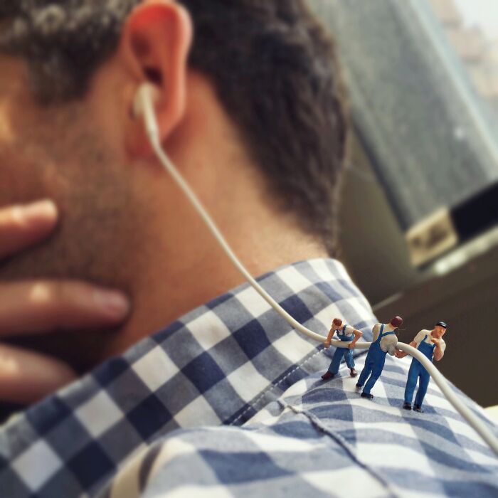 Miniatures of workers pulling earphone cord on a man's checkered shirt, creating a secret world scene.