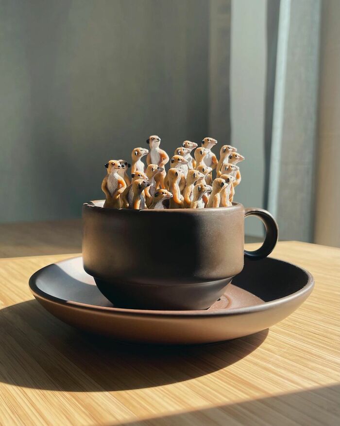 Miniature meerkats gathered in a brown teacup on a sunny table.