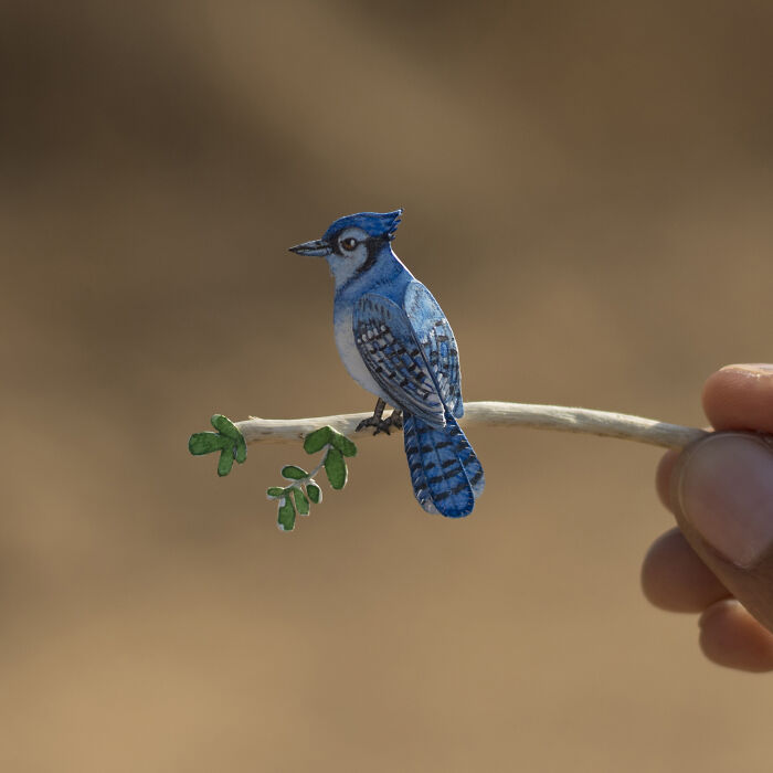 Miniature bluejay sculpture on branch, showcasing intricate details of secret worlds.