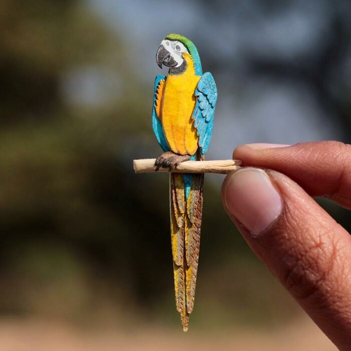 Miniature parrot sculpture held between fingers, showcasing stunning detail and craftsmanship.
