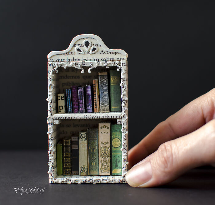 Miniature bookshelf with detailed tiny books, held by a hand, showcasing intricate craftsmanship.