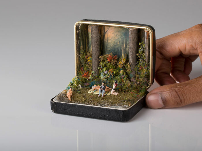Miniature forest scene in a box with tiny figures, held by a hand.